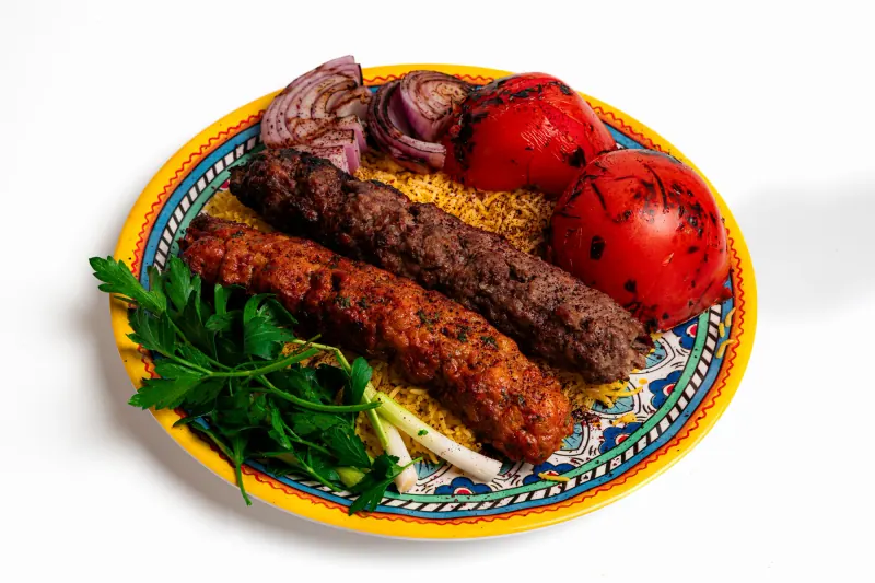 Two kabobs over yellow rice with grilled tomato and onion