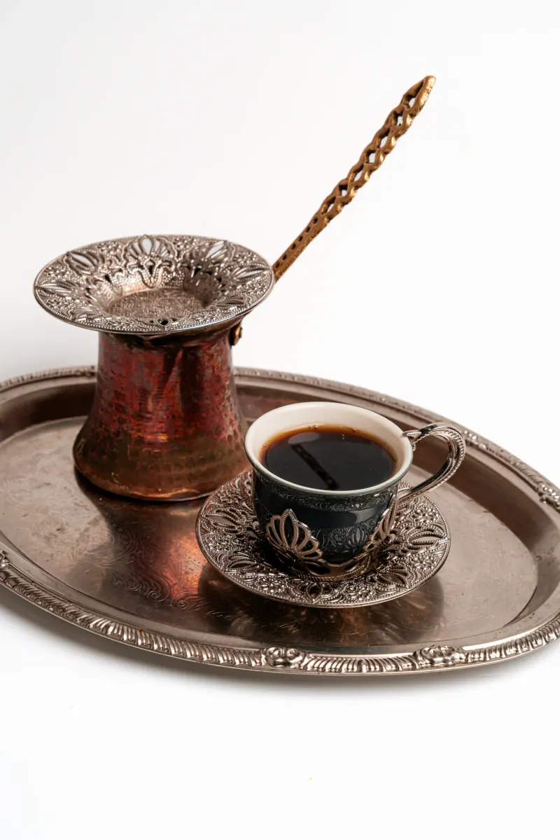 A copper coffee pot and a patterned cup on a silver tray